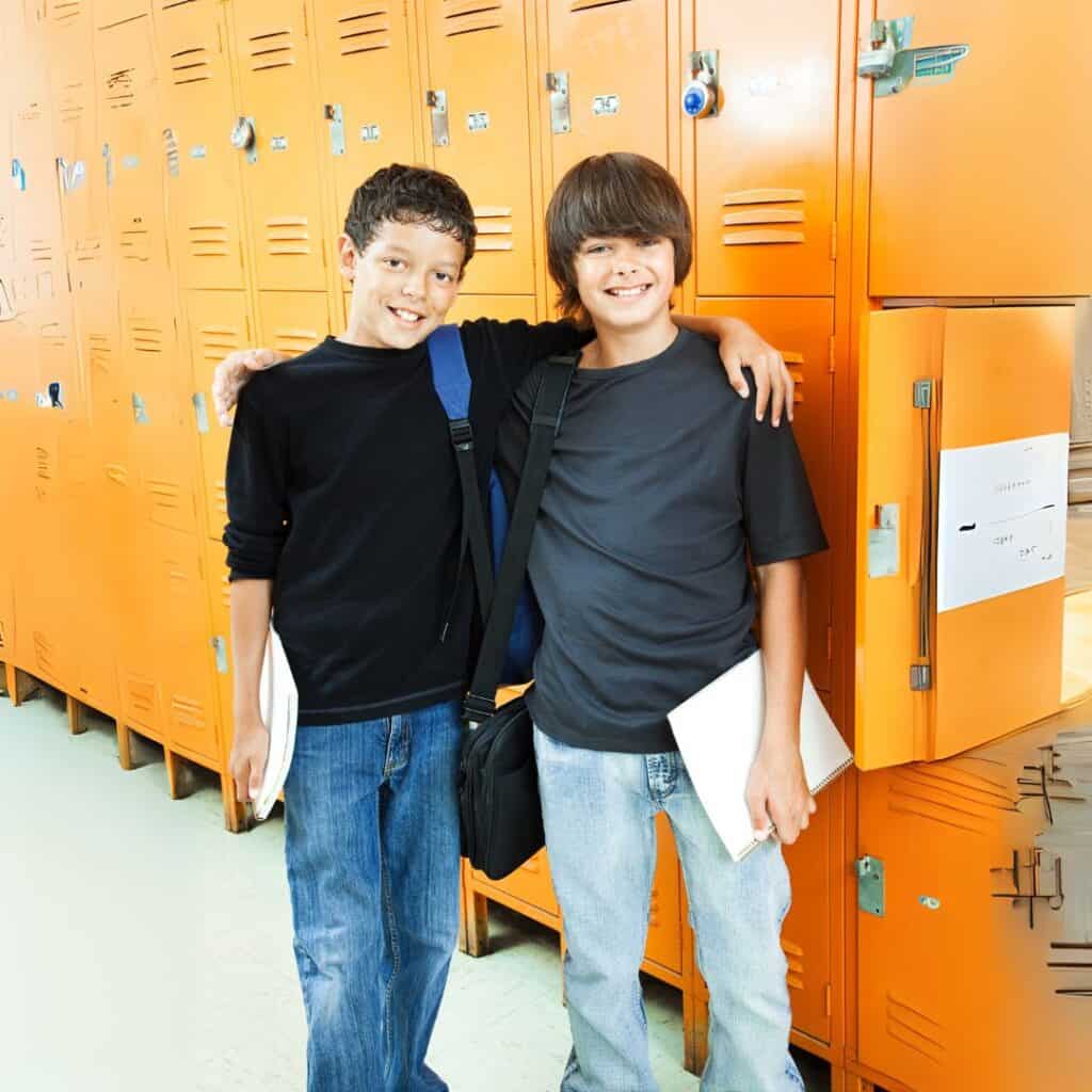 Photograph of two middle school age boys in a hallway in front of a row of school lockers. The boys have their arms around each other and they are smiling. Used to show friendship for the post Praying for my Grandson.