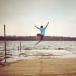 Photo of a teen age boy jumping off a pier into a lake. He has his arms and legs spread in a joyful manner. Used to illustrate the post Praying for my Grandson, to show an activity a boy might like to do.