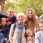 A photograph of a family consisting of grandparents, parents, and 4 children who range in age from 6 -16. Used to illustrate a post about how to pray for your grandchildren's faith. The family is posed in front of a tree with a forest background. They are wearing shades of blue and are smiling.