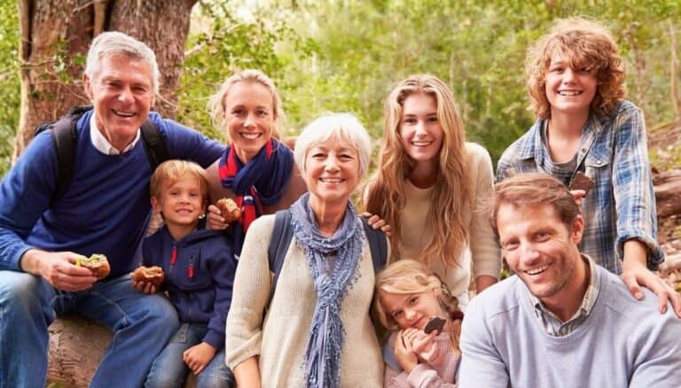 A photograph of a family consisting of grandparents, parents, and 4 children who range in age from 6 -16. Used to illustrate a post about how to pray for your grandchildren's faith. The family is posed in front of a tree with a forest background. They are wearing shades of blue and are smiling.