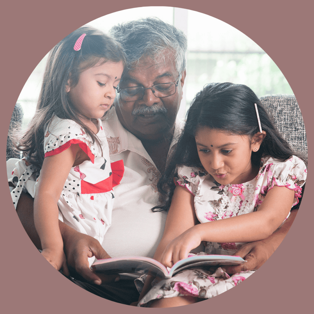 Photo of an Asian grandfather and 2 granddaughterUsed to illustrate the post How to pray for your grandchildren's faith.s reading a book on the couch.