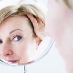 Photo of a woman in her 60's looking in a mirror. The mirror is centered, and the woman's face is visible in it. She looks curious and slightly apprehensive. Used to illustrate the blog post Being a Grandma - How Your Identity May Change.