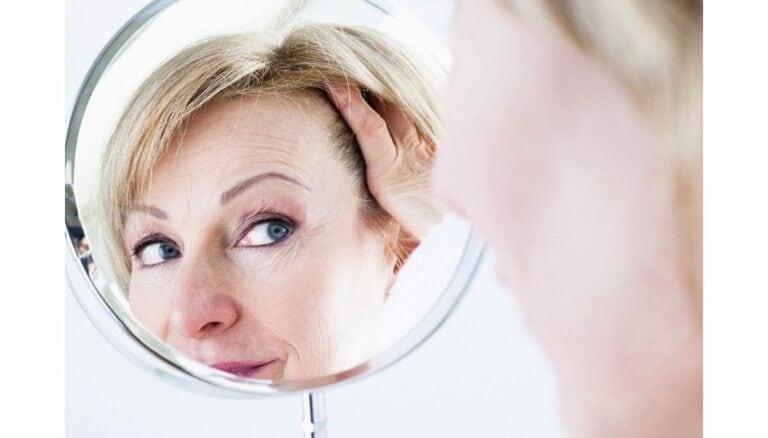Photo of a woman in her 60's looking in a mirror. The mirror is centered, and the woman's face is visible in it. She looks curious and slightly apprehensive. Used to illustrate the blog post Being a Grandma - How Your Identity May Change.