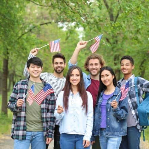 A group of 6 teenagers in a park holding small USA flags. There are 4 boys and 2 girls of different races. All are smiling and waving their flags. Used as an in-post picture for the National Day of Prayer blog post.