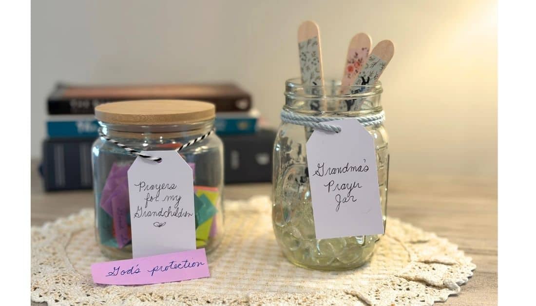 Photo of 2 prayer jars. They are sitting side by side on a doily with 3 books stacked behind them. The jar on the right has a tag that says Grandma's Prayer Jar. The prayer jar on the left has a tag that says Prayers for my Grandchildren.