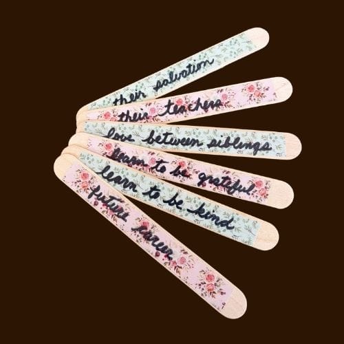 This photo has 6 popsicle sticks. Each stick has a piece of washi tape on it with a prayer request written on it. These sticks would be added to a prayer jar.