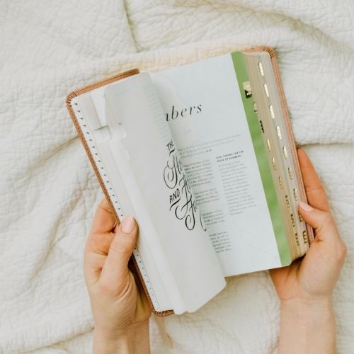 Photo of a woman's hands holding a Bible. The woman is flipping through the Bible. The background looks like a blanket. Used to illustrate the post 24 Bible Verses About Grandparents.