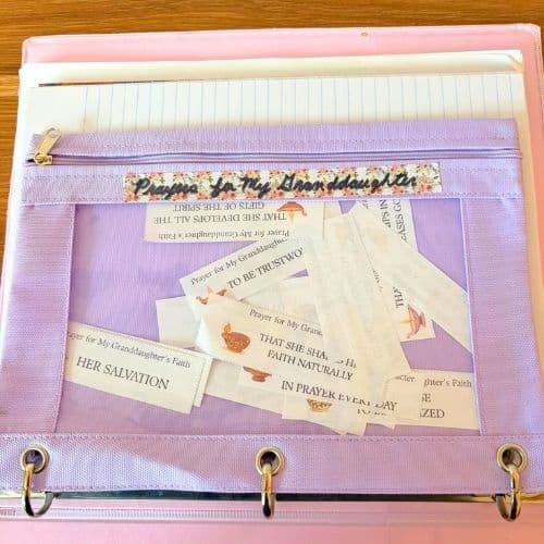 Photo of a pencil bag filled with prayer slips. The bag is in a 3-ring binder. The label on the pencil bag says Prayers for My Granddaughter. Used to illustrate what to do with prayer slips after use for the post Prayers for a Granddaughter.